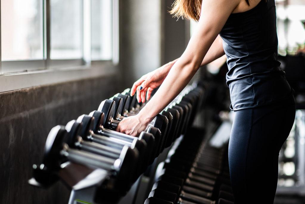 Woman in workout clothing selecting dumbells from a weight rack for a CrossFit Workout