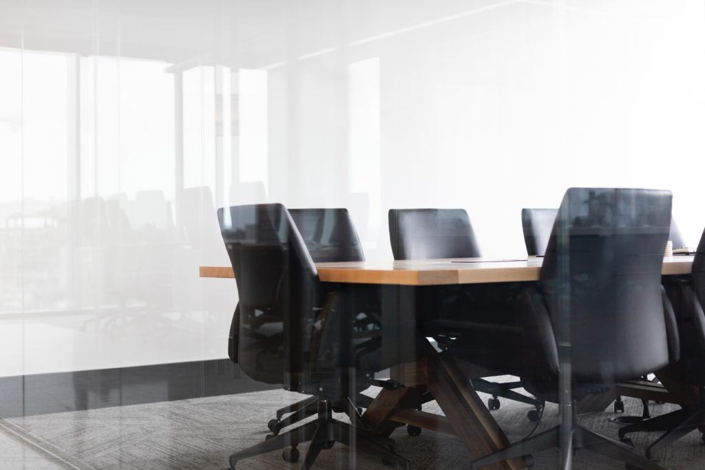 Group of black leather chairs arranged around a conference table in a glass-walled conference room