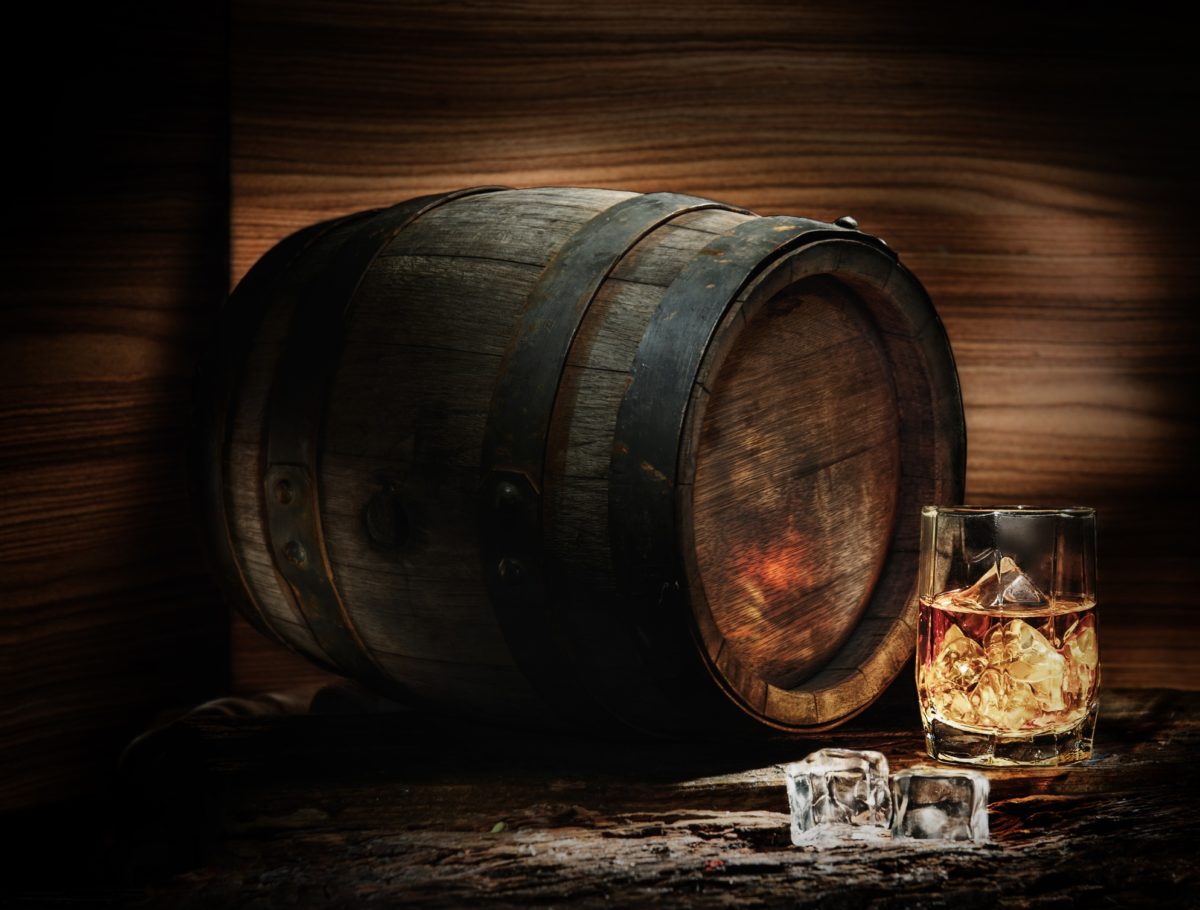 Whisky barrel sitting next to a crystal glass full of whiskey in a dimly lit distillery