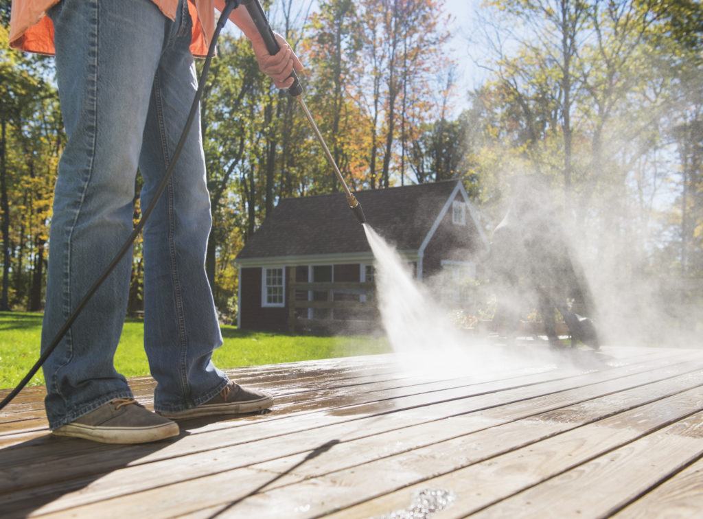 Closeup of a man in jeans power washing a wooden deck on a sunny day
